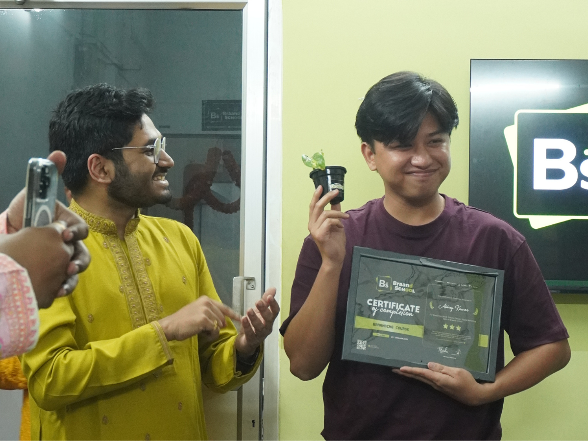 Student Abhay Kumar smiling while holding his Branding Course certificate and a small plant gift, with a mentor clapping in the background.