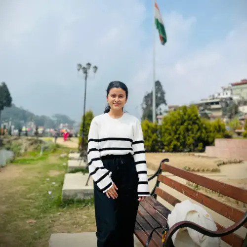 A close-up portrait of a young woman with long, highlighted brown hair, wearing a thick grey scarf and illuminated by warm, golden sunlight.